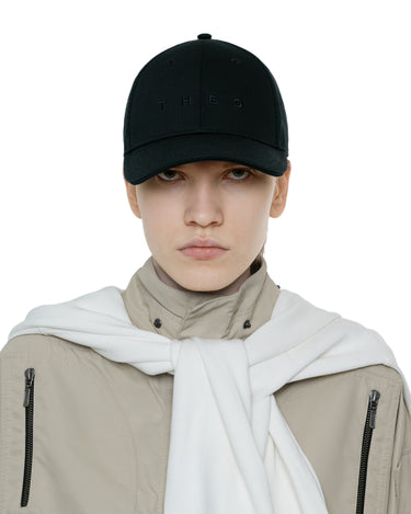 Black baseball cap with small front logo lettering, worn with a white hooded scarf