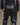 Men's black faux-leather trousers close-up with belt and stitched front pockets