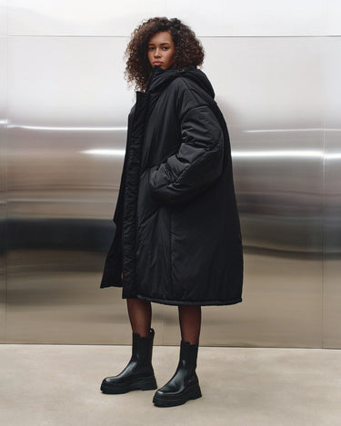 Black hooded puffer coat side view with structured quilting and long sleeves