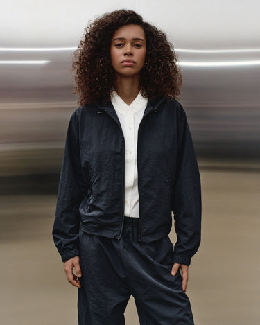 Dark hooded wind shell jacket on model, front view with open zipper over white tee.