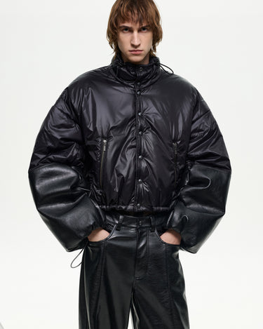 Men's black puffer jacket with glossy finish, oversized sleeves and snap-front closure, worn