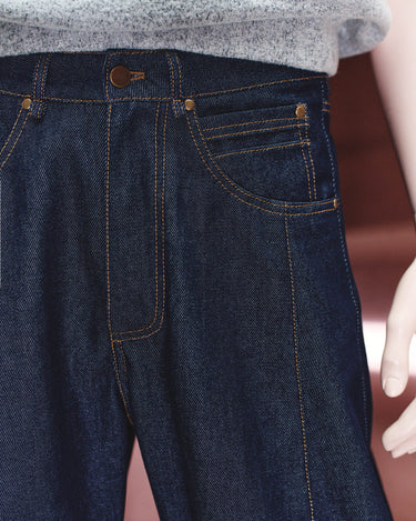Dark navy denim jeans detail with button closure and contrast orange-stitched pockets