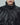 Close-up of the black puffer jacket's high collar, snap-button front and zip pockets