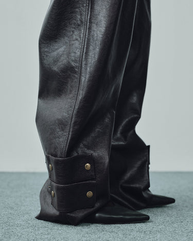 Close-up of black faux leather pant cuff with two snap button tabs