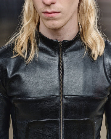 Men's black leather-look jacket detail: center zipper and stitched chest panels