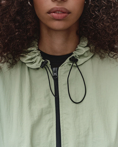 Light green hooded wind shell jacket close-up with drawcord and black zipper