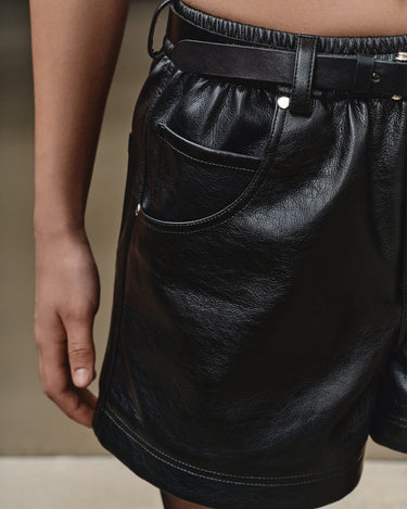 Black faux-leather mini shorts close-up with belt loops and front seam