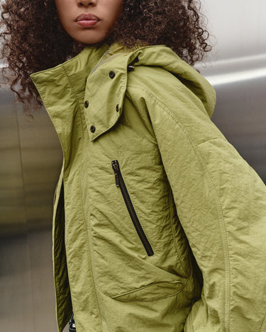 Green nylon TMBY jacket close-up with drawcord hood and zip pocket