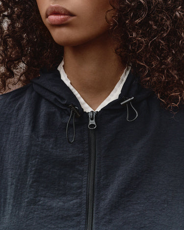 Dark wind shell jacket front with zip, hood drawstrings, and white shirt collar