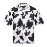Camp shirt close-up: button-front collar, black abstract print on white; THEO label.