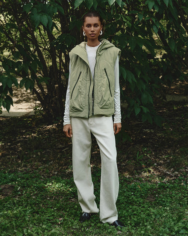 Light green hooded puffer vest worn over long sleeves; front zip and hood.