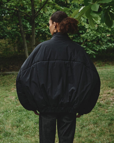 Back view of padded bomber jacket in dark color with ribbed collar and elastic cuffs.